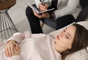 Woman sitting down with her eyes closed while doctor is writing down notes next to her